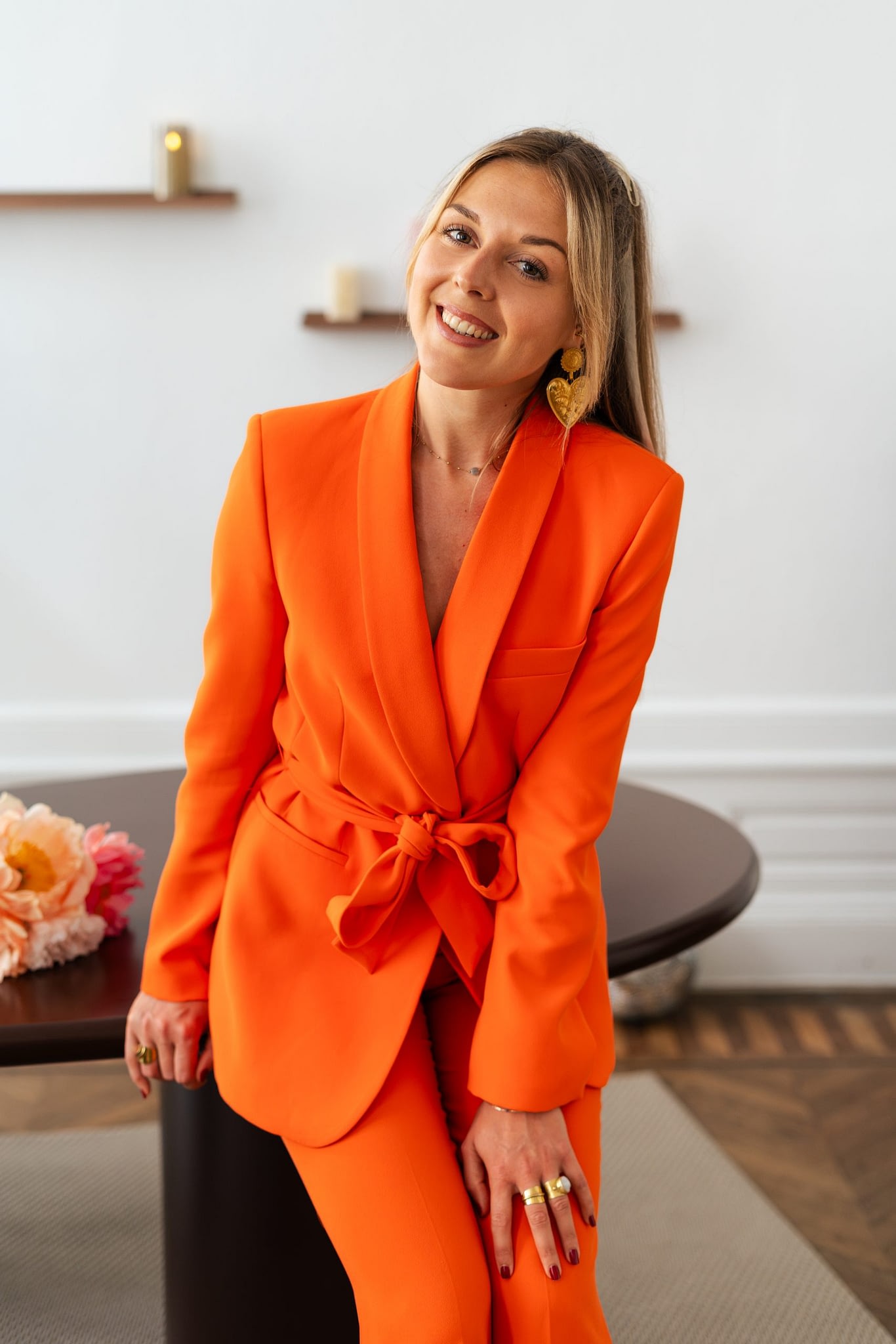 Portrait de Meije en tailleur orange, appuyée contre une table dans un intérieur lumineux